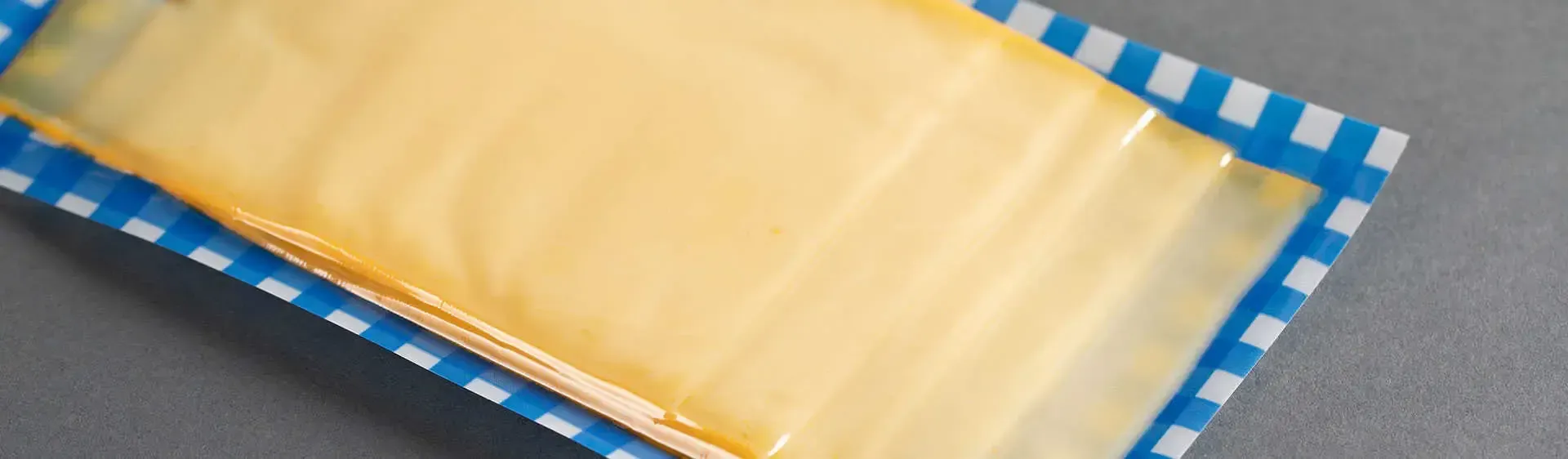 Ein gelbes, rechteckiges Dessert auf einem blau-weiß gemusterten Tablett auf grauer Oberfläche.