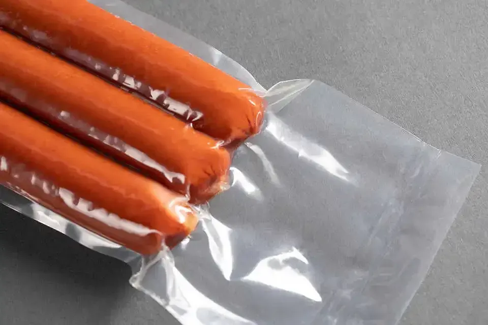 Vier orangefarbene Würstchen in einer durchsichtigen Plastikverpackung auf einer grauen Oberfläche