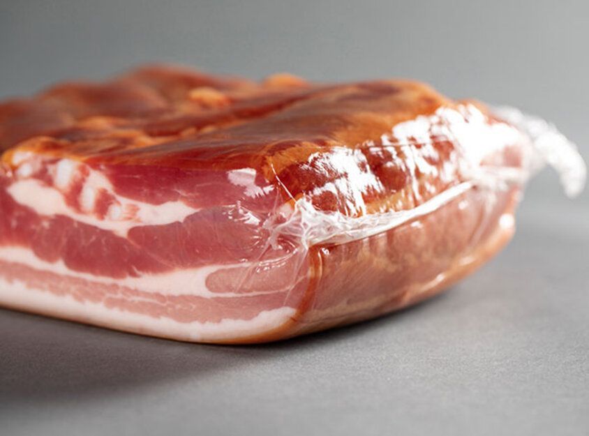 Dünn geschnittenes, gepökeltes Fleisch, in Plastik verpackt, auf einer grauen Oberfläche