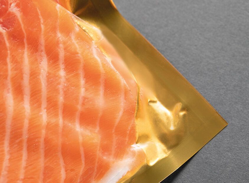 Rohes Lachsfilet auf goldener Verpackung vor grauem Hintergrund