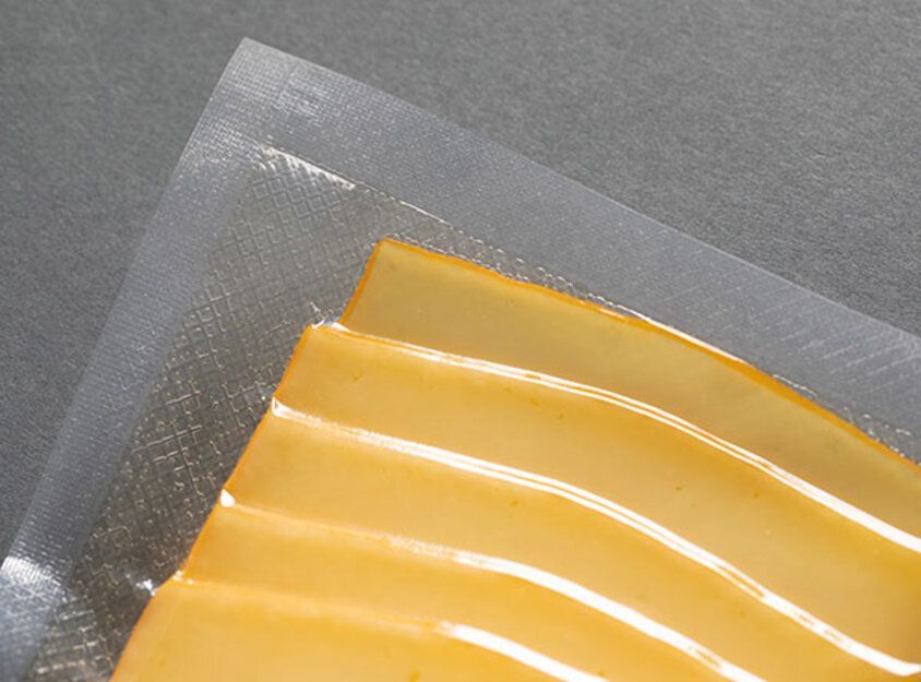 Nahaufnahme von orangefarbenen Käsescheiben in durchsichtiger Plastikverpackung auf grauer Oberfläche