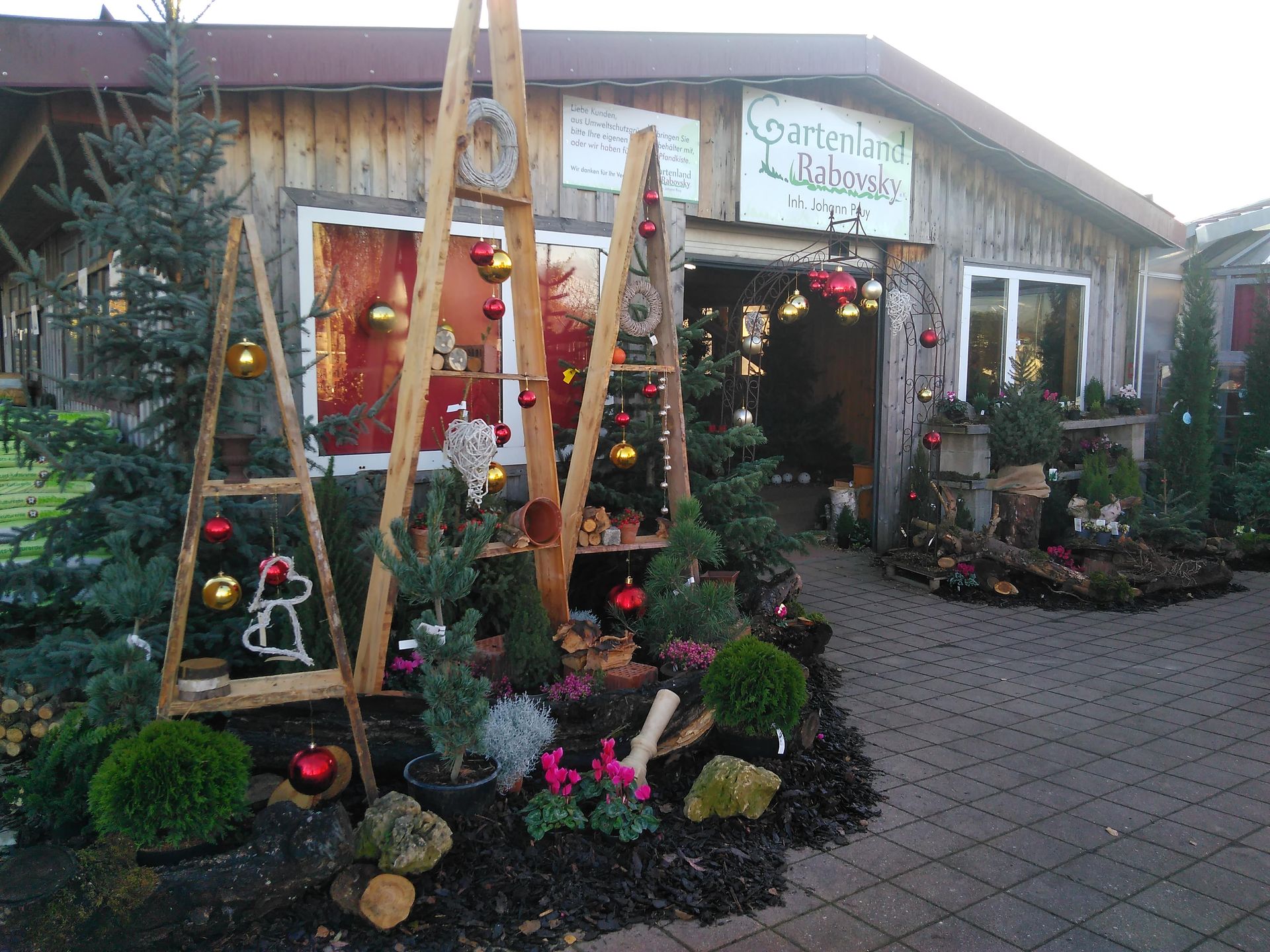 Eingang zum Weihnachtsmarkt mit Holzleitern, Ornamenten und immergrünen Bäumen.