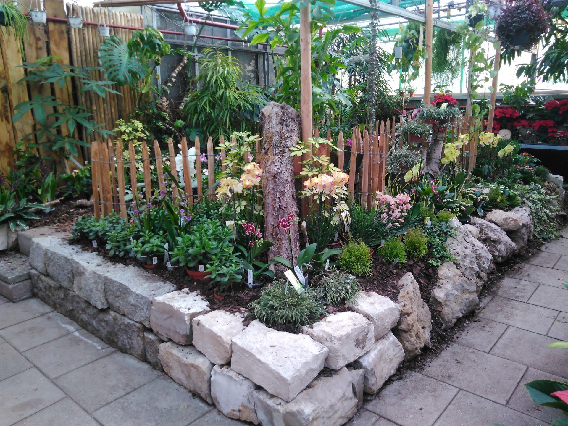 Ein Gartenbeet mit Steinrand und kleinem Holzzaun, gefüllt mit verschiedenen Pflanzen und Blumen.