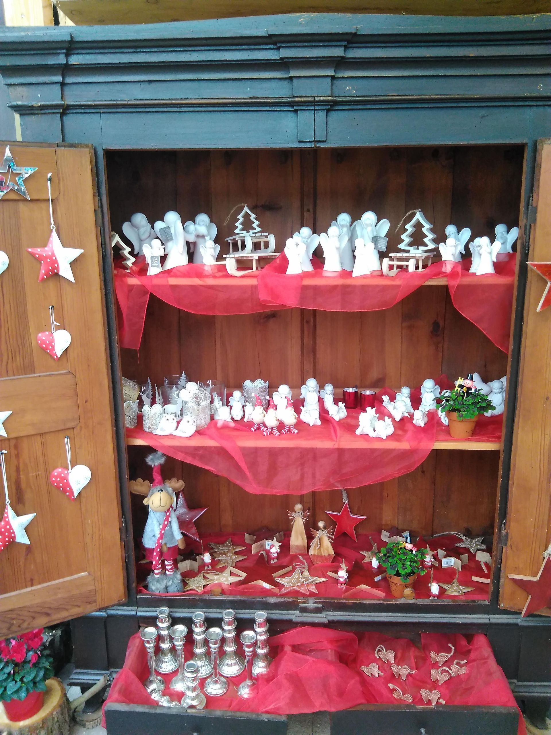 Weihnachtsdekoration im Holzschrank: Engel, Sterne und Ornamente auf Regalen mit rotem Stoff.
