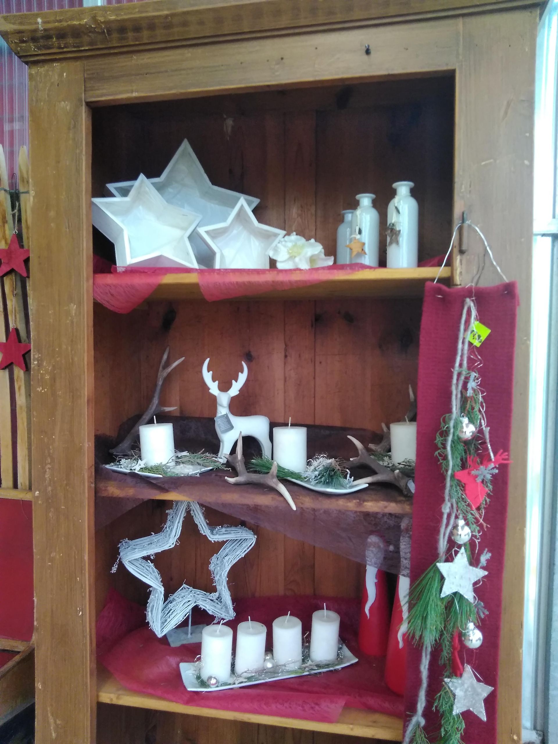 Holzvitrine mit Weihnachtsdekorationen, darunter Sterne, Kerzen und Hirschfiguren.