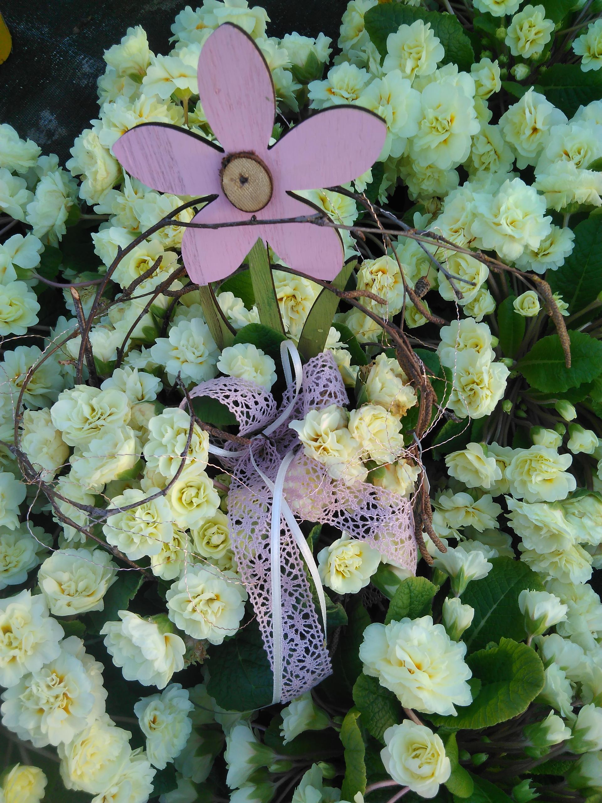 Rosa Holzblumen- und Schleifendekoration mit weißen und gelben Blumen.
