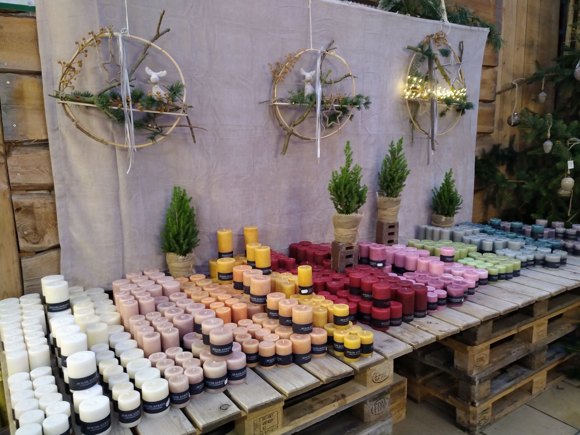 Eine Ausstellung bunter Kerzen auf Holzpaletten mit dekorativen Kränzen in einem Geschäft.