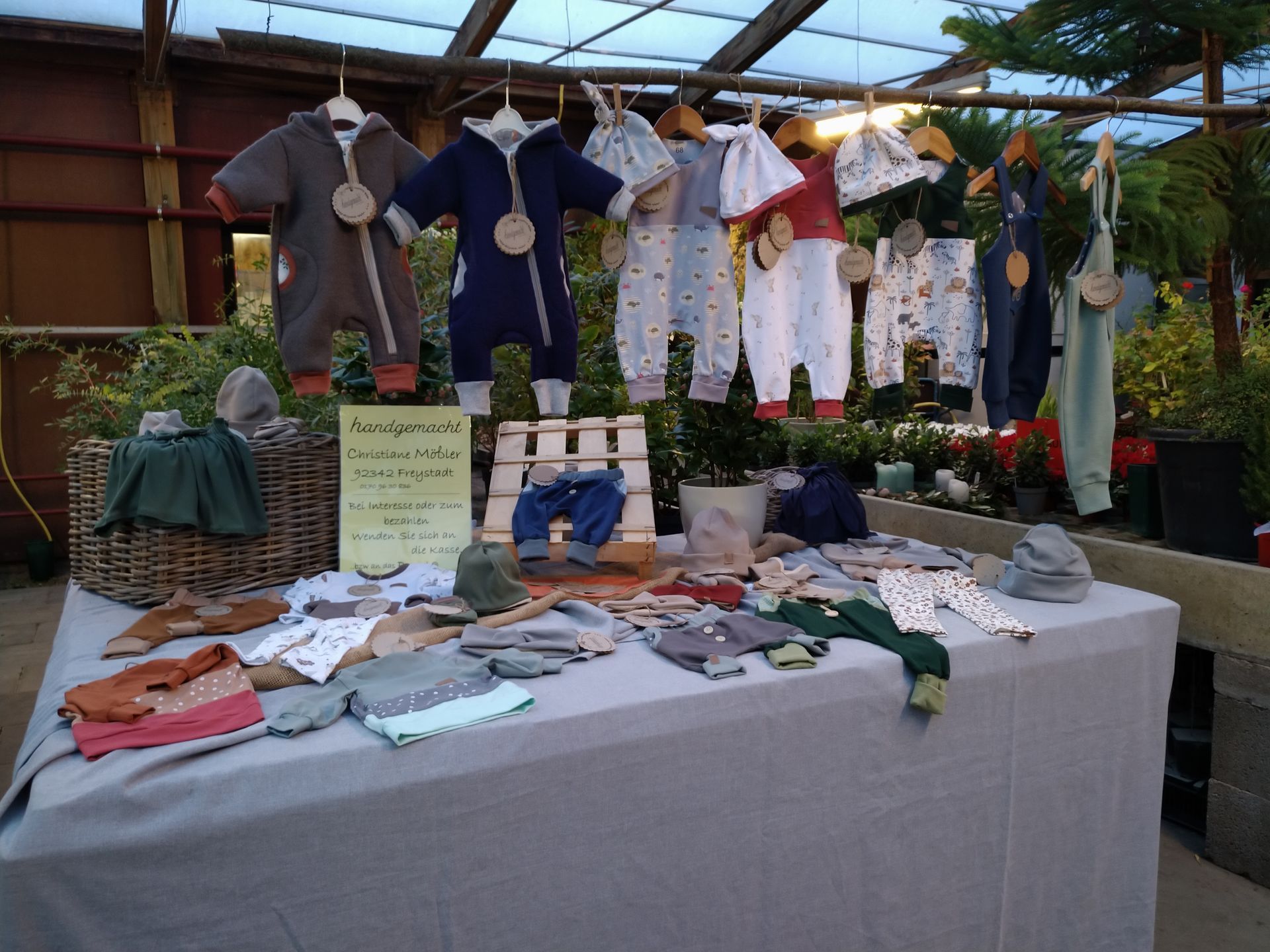 Kleiderständer mit Babykleidung, hängend und auf einem Tisch, in einem Gewächshaus.