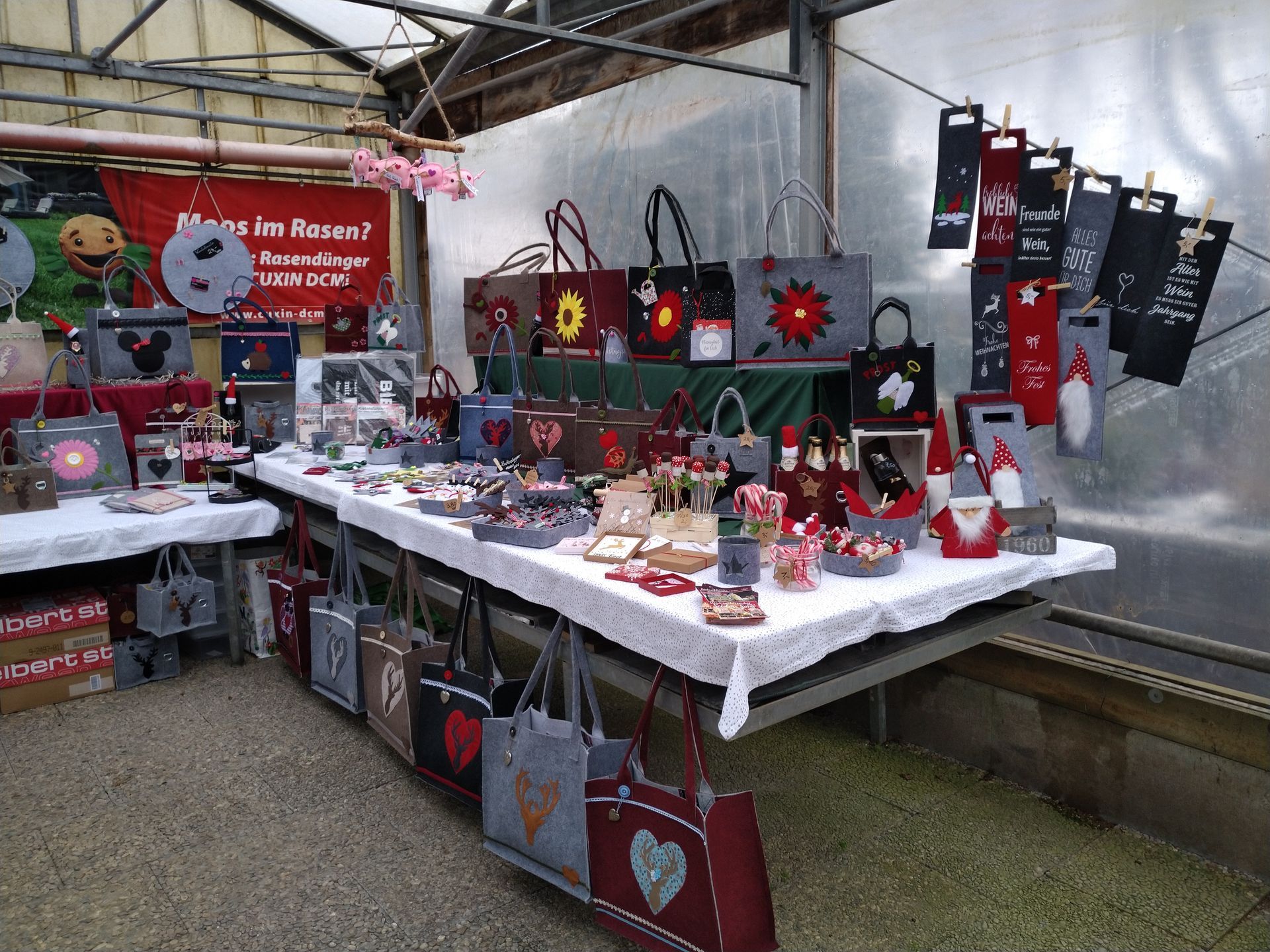 Ausstellungstisch für einen Kunsthandwerkermarkt mit handgefertigten Taschen, Geschenken und Dekorationen in einem Gewächshaus.