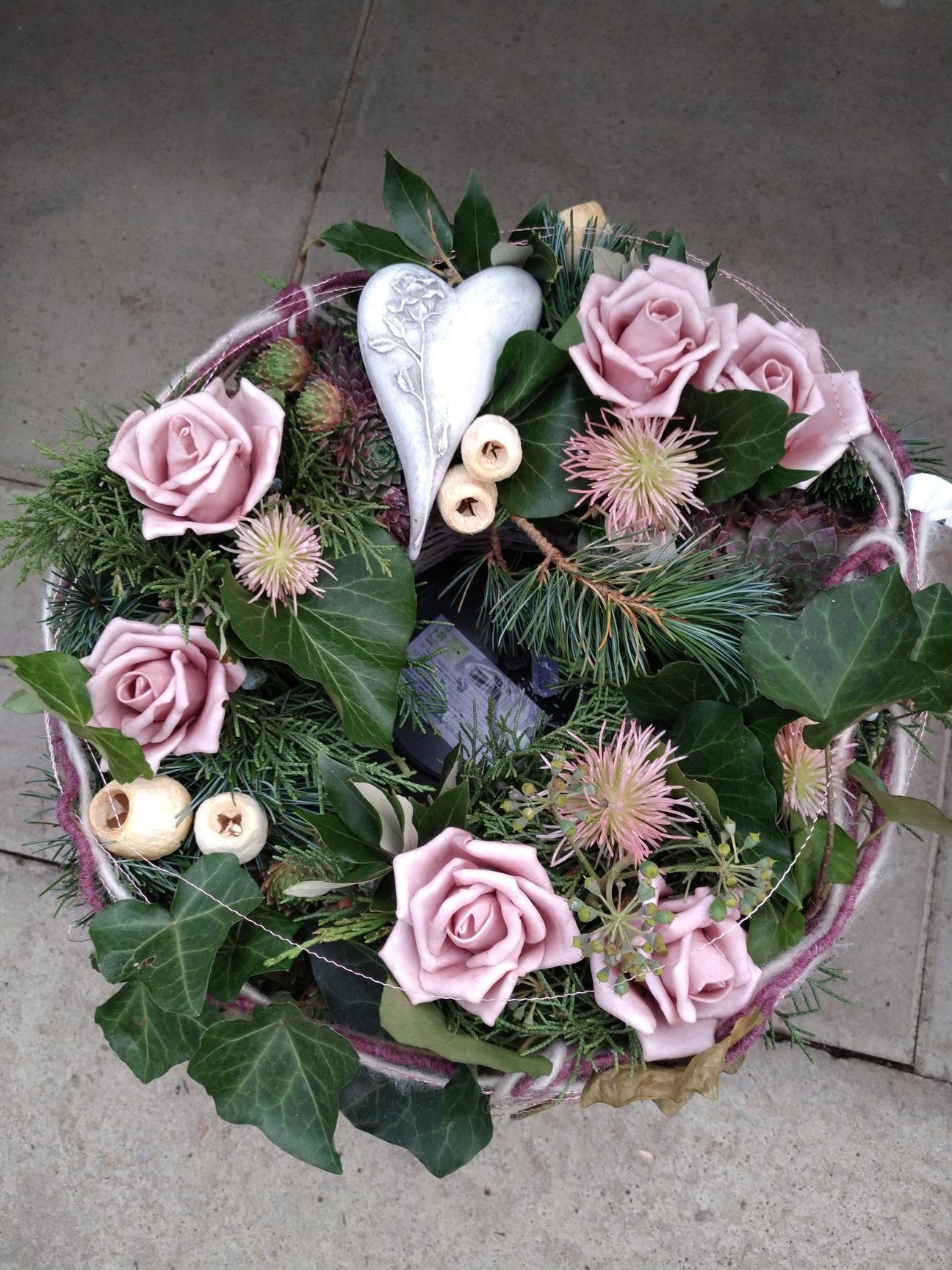 Kranz mit rosa Rosen, grünem Laub, einem weißen Herz und dekorativen Elementen.