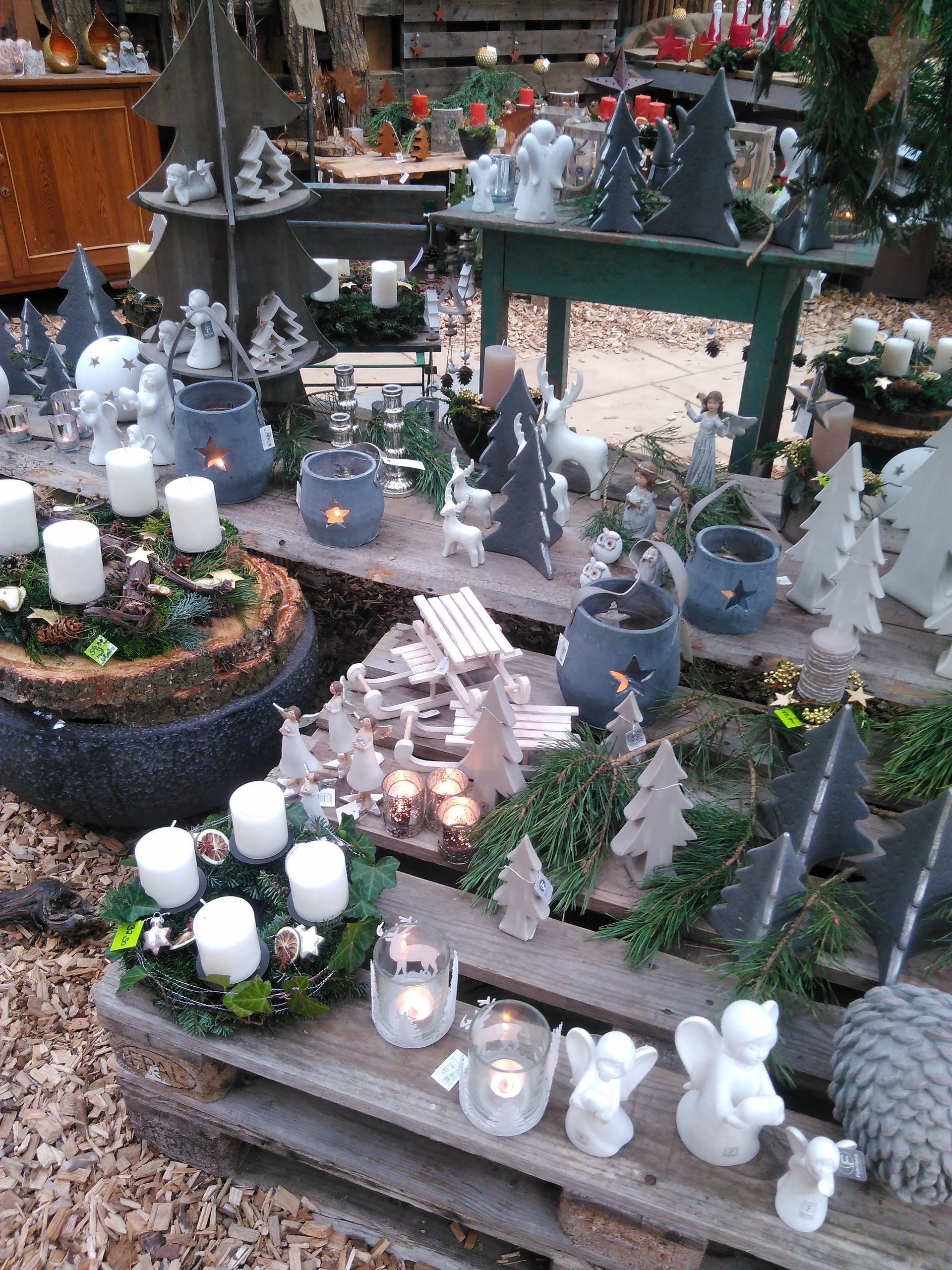 Weihnachtsdekorationen zu verkaufen: Kerzen, Keramikfiguren, Holzbäume, auf Paletten arrangiert.