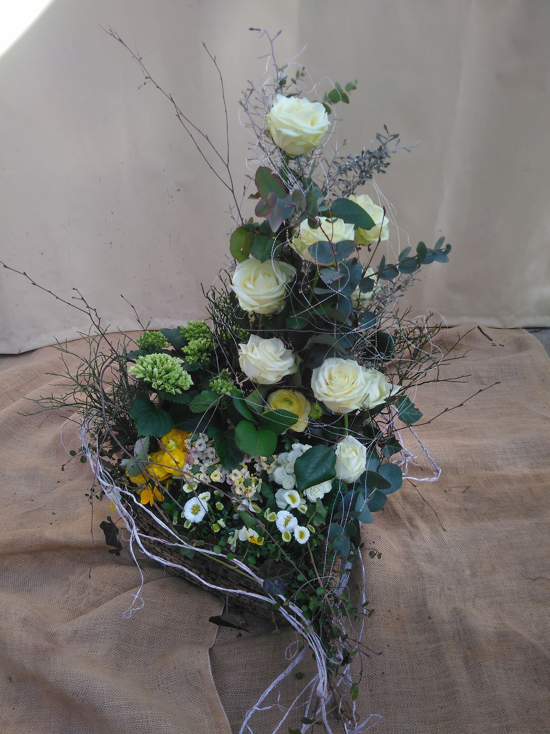 Weiße Rosen und Grünpflanzenarrangement auf einem Sackleinenhintergrund.