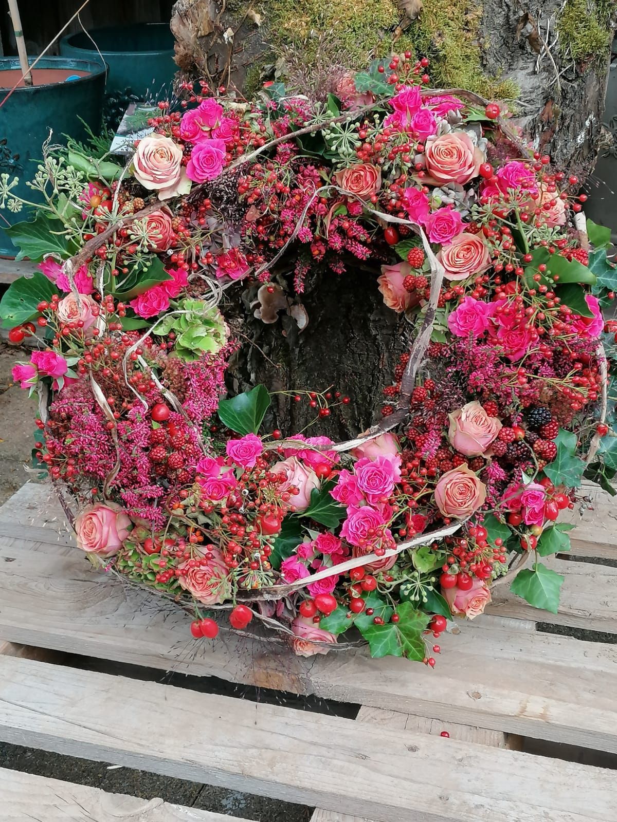 Kranz aus rosa und roten Blumen und Beeren auf einer Holzpalette.