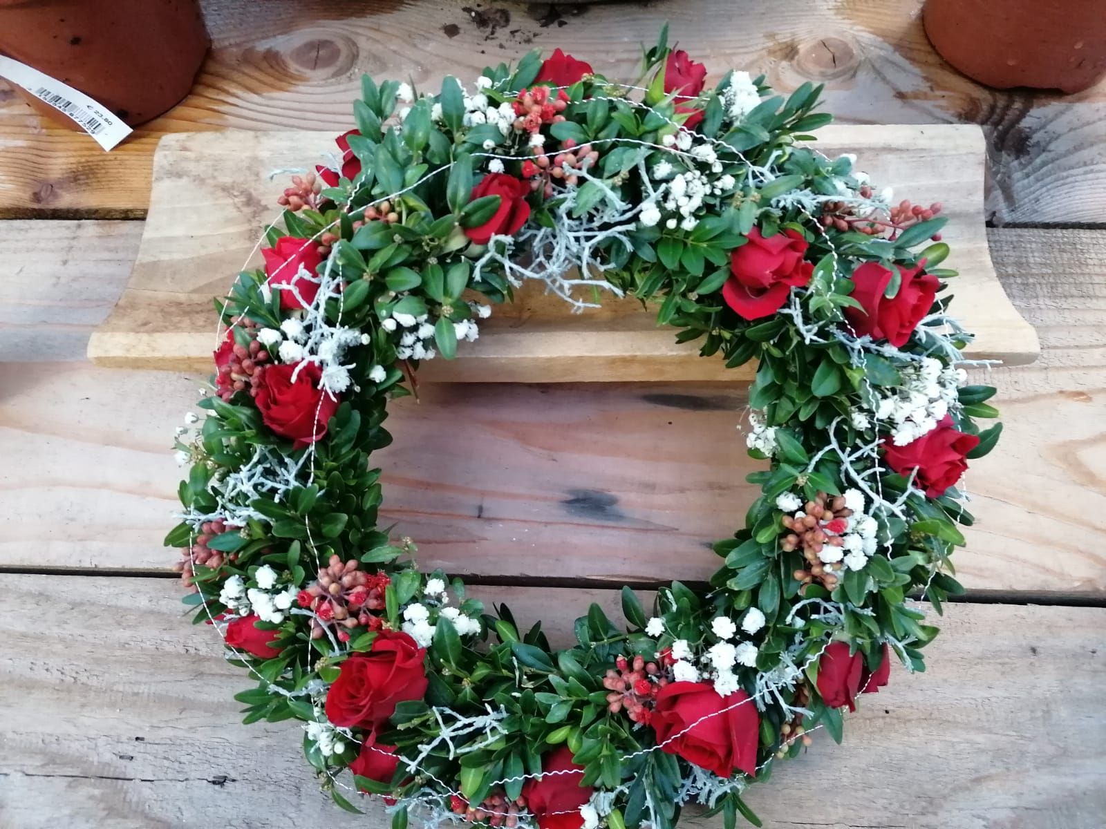 Kranz mit roten Rosen, weißen Zweigen und grünem Laub auf einer Holzoberfläche.