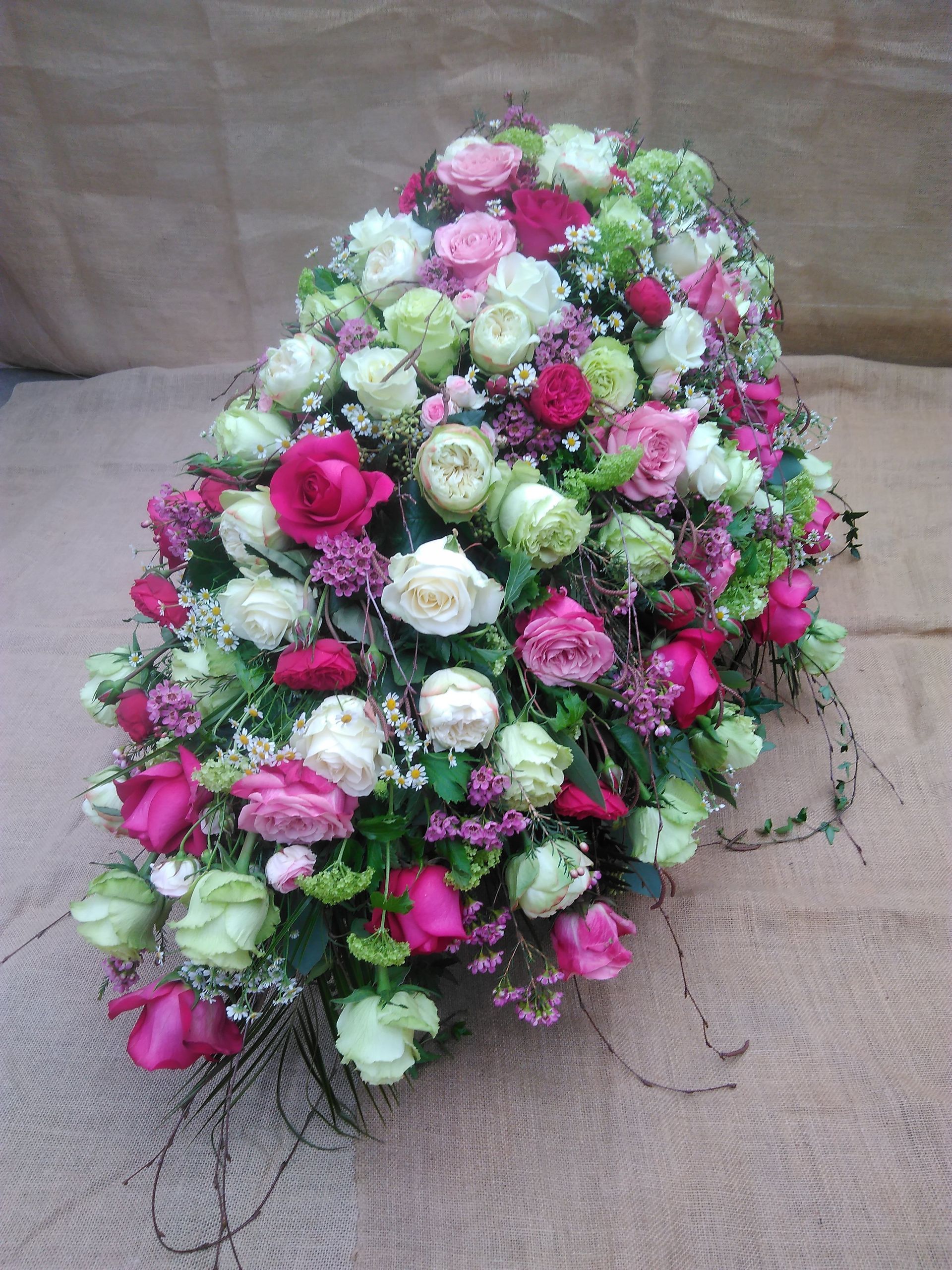 Trauergesteck aus weißen, rosa und roten Rosen mit Grün auf hellbraunem Hintergrund.