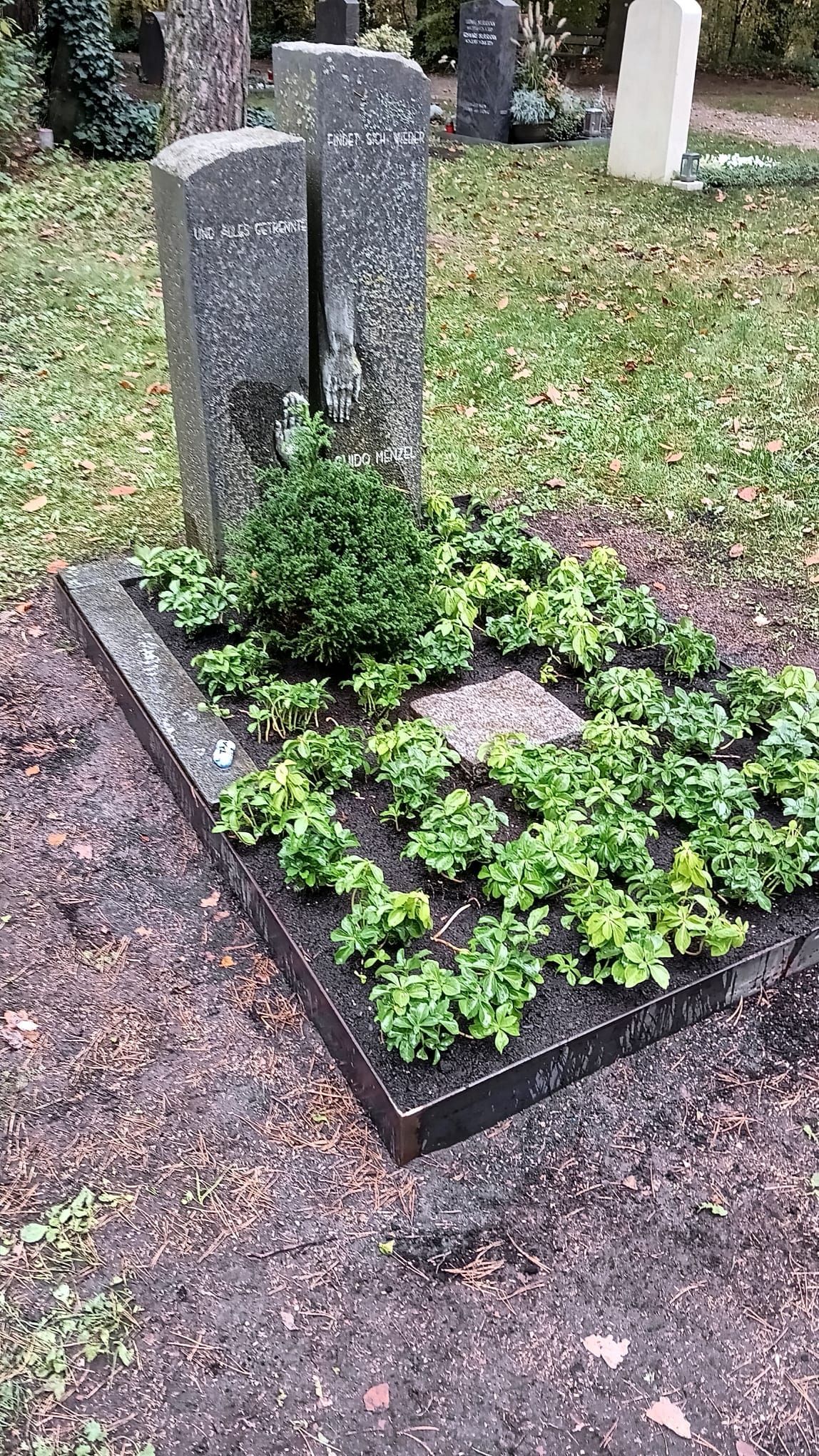 Grab auf einem Friedhof mit Steinmarkierung und umgebendem Grün.