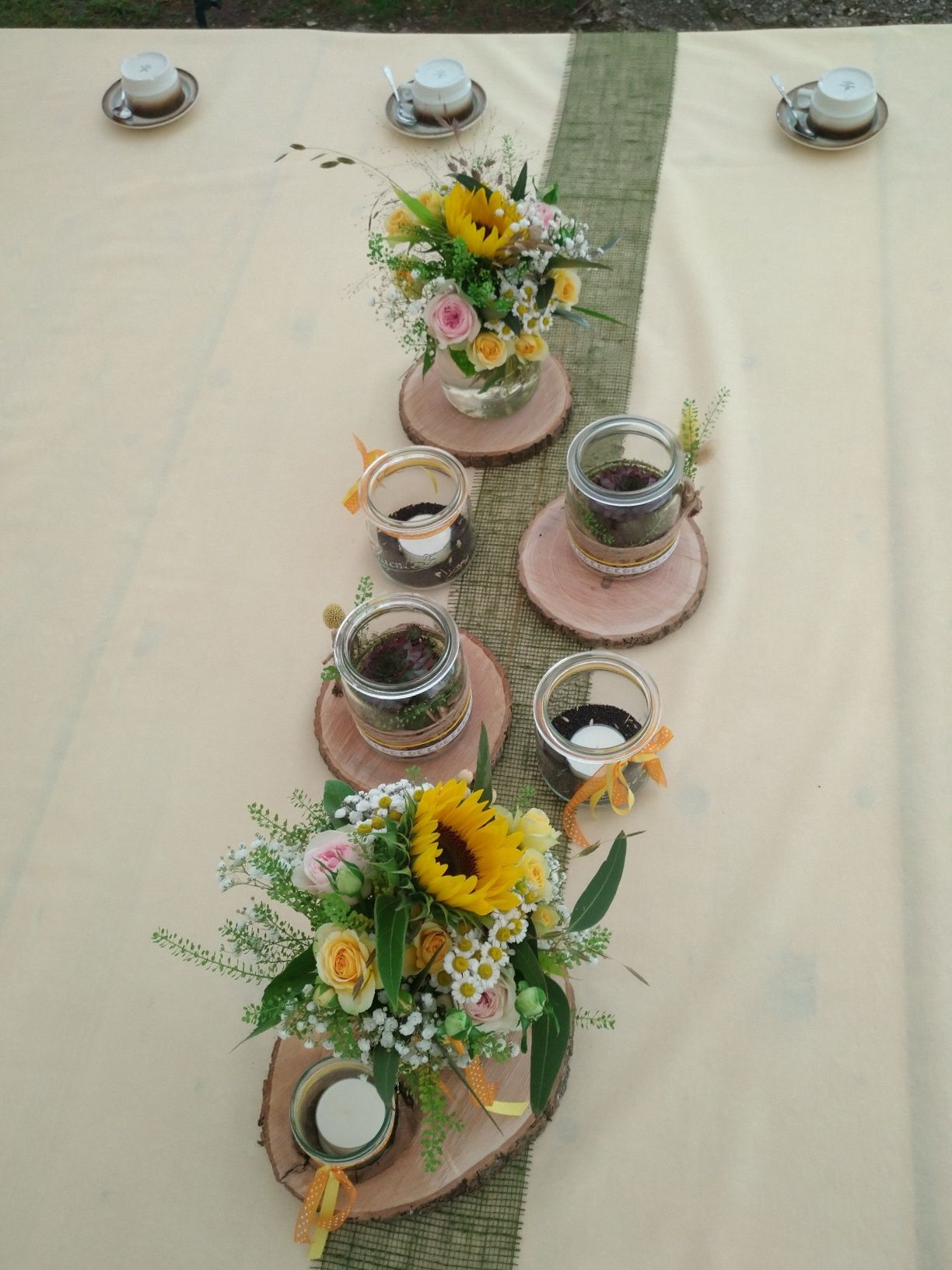 Tischdekoration mit Sonnenblumen-Tischdekorationen, Kerzen und Teetassen auf einer cremefarbenen Tischdecke.