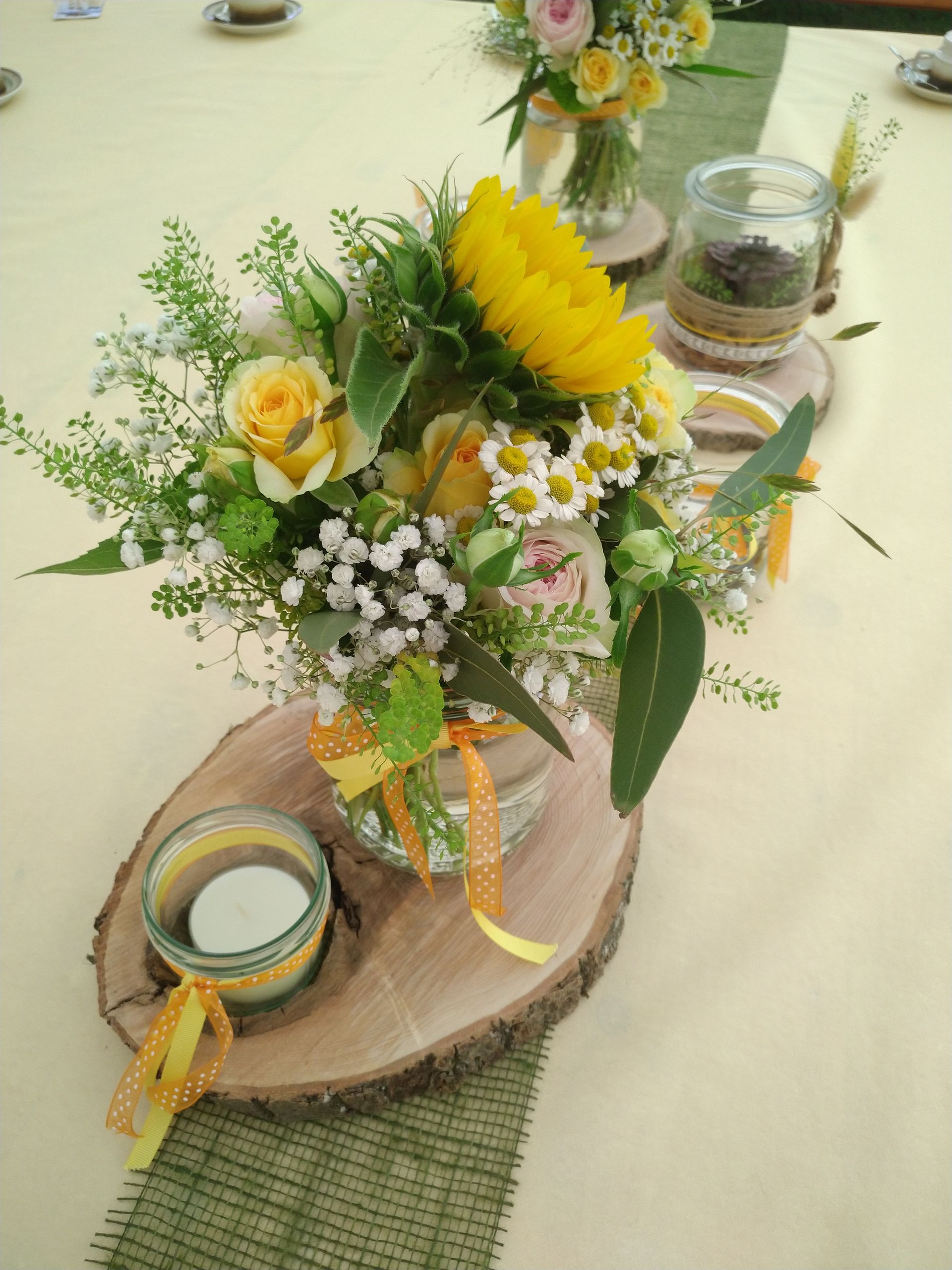 Tafelaufsatz mit gelben Blumen, Sonnenblumen und Kerzen auf einer Holzplatte; Tischdekoration.