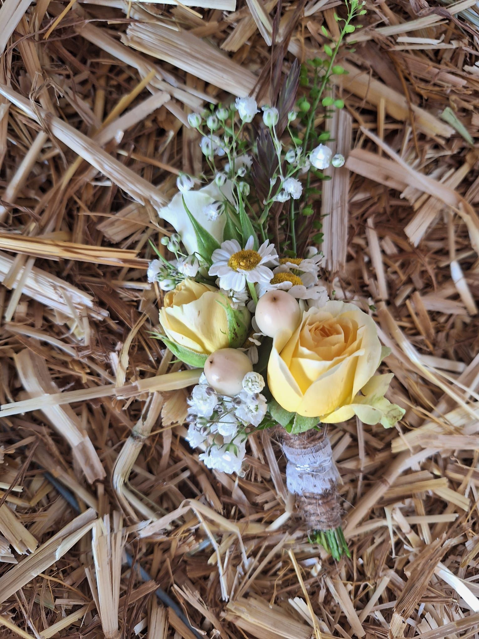 Ansteckblume aus gelben Rosen, Gänseblümchen und Schleierkraut, in Schnur und Spitze gewickelt, auf einem Strohbett.