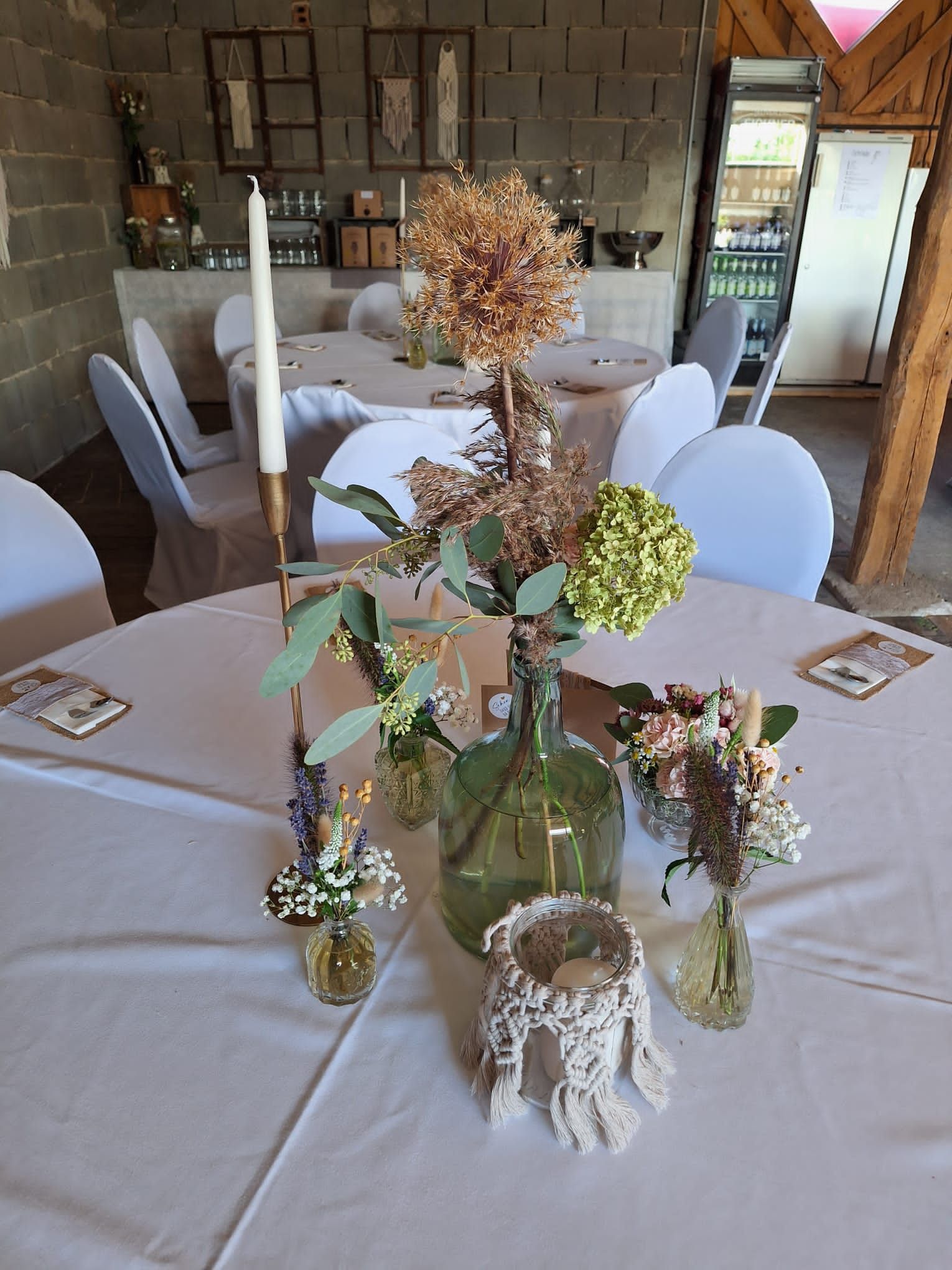 Tischdekoration für den Hochzeitsempfang mit getrockneten Blumen in grünen Glasflaschen.