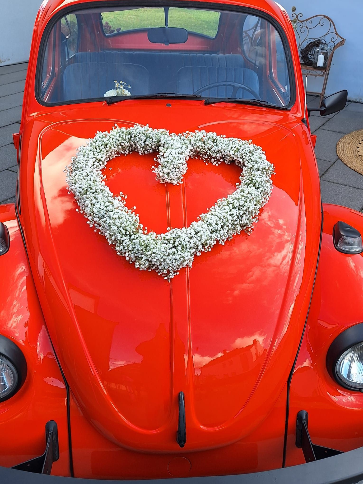 Roter Volkswagen Käfer, geschmückt mit einem herzförmigen Blumenkranz für eine Hochzeit.