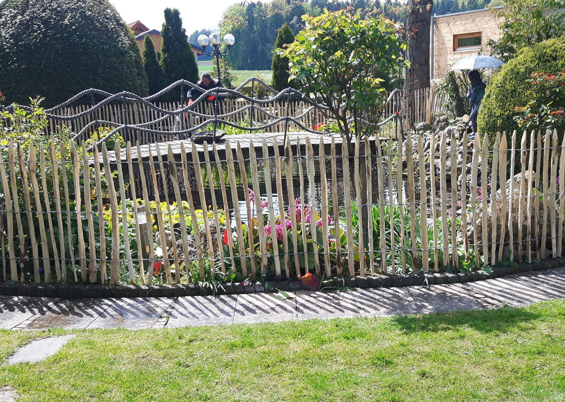 Ein niedriger Holzzaun umgibt ein Gartenbeet mit bunten Blumen, sonniger Tag.