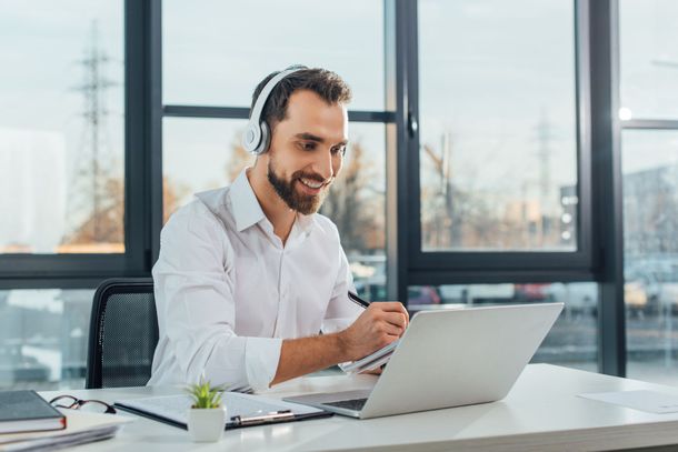 Ein Mann mit Kopfhörern sitzt an einem Schreibtisch und benutzt einen Laptop.