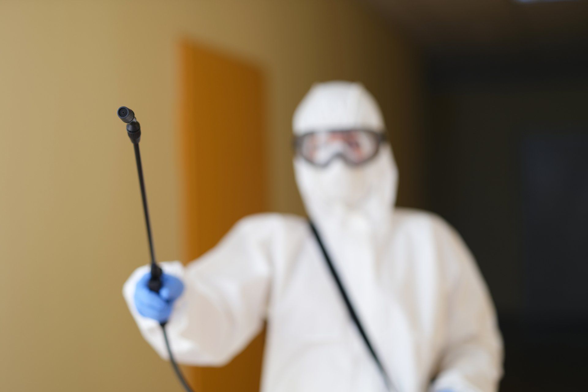 Personne en combinaison de protection blanche et masque tenant un pistolet pulvérisateur à l'intérieur.
