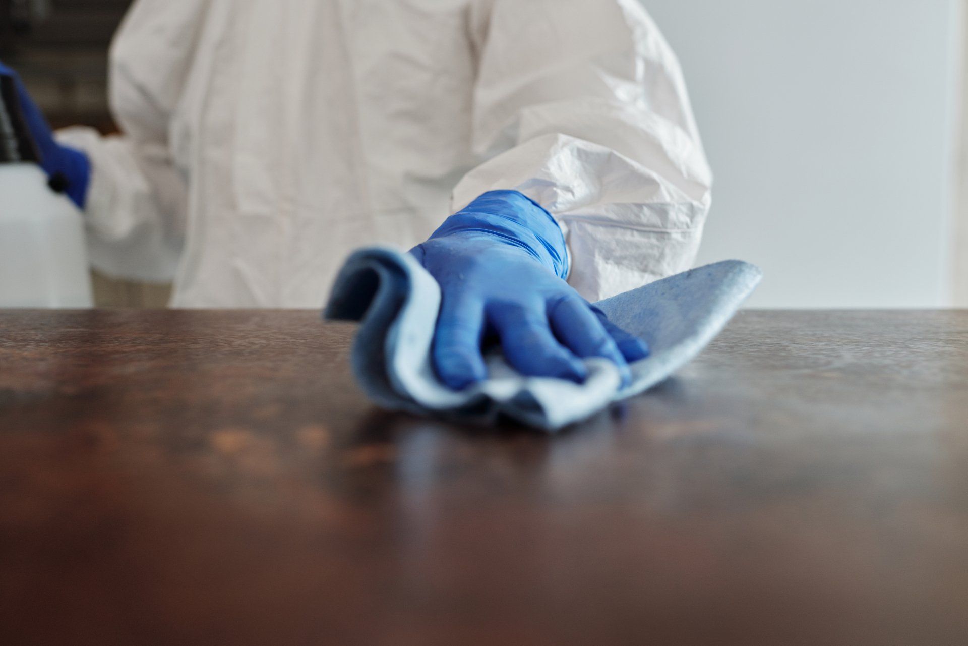 Main gantée essuyant une table en bois avec un chiffon bleu, gros plan dans une scène de nettoyage