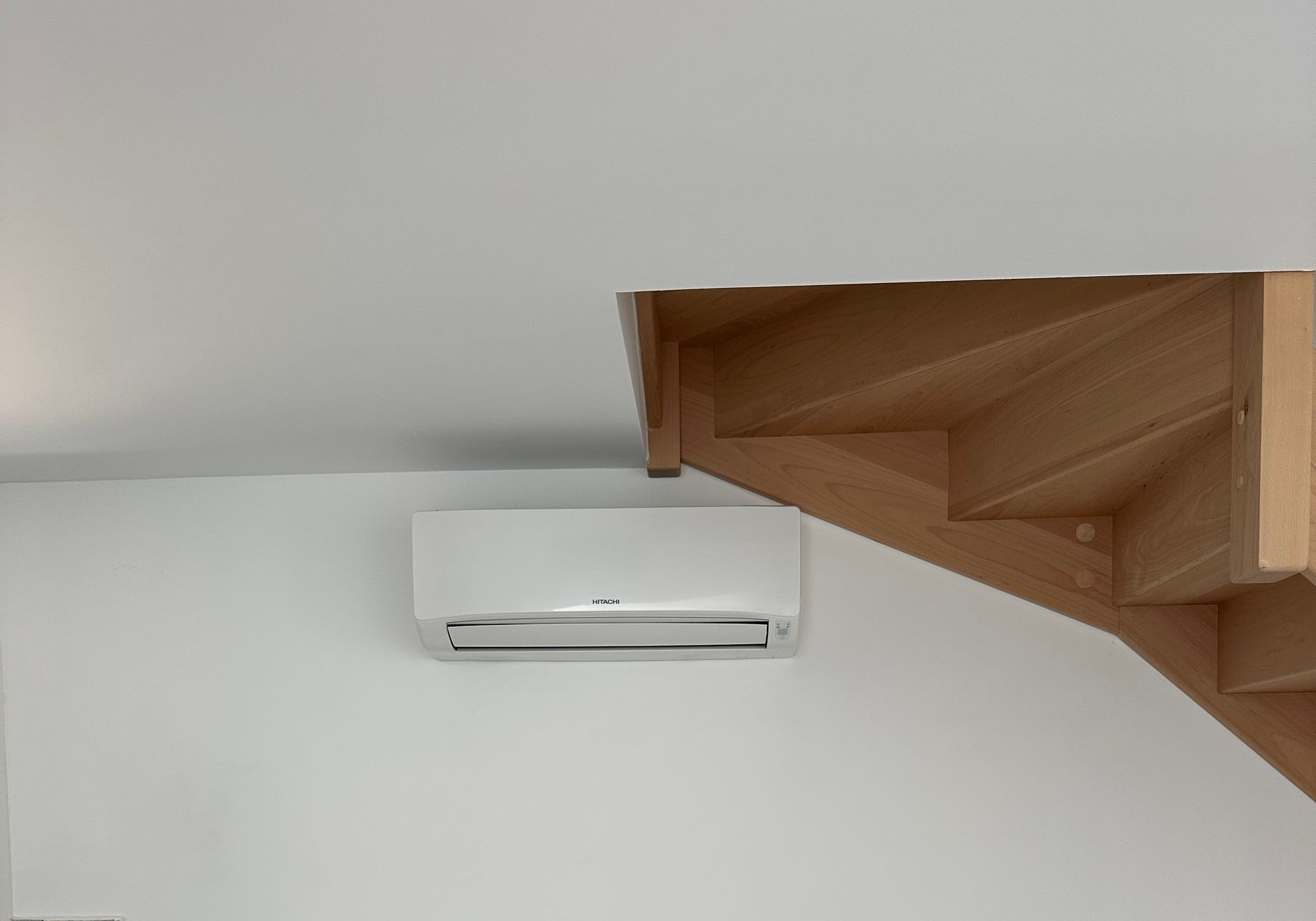 Climatiseur mural à côté d'un escalier en bois, contre un mur.
