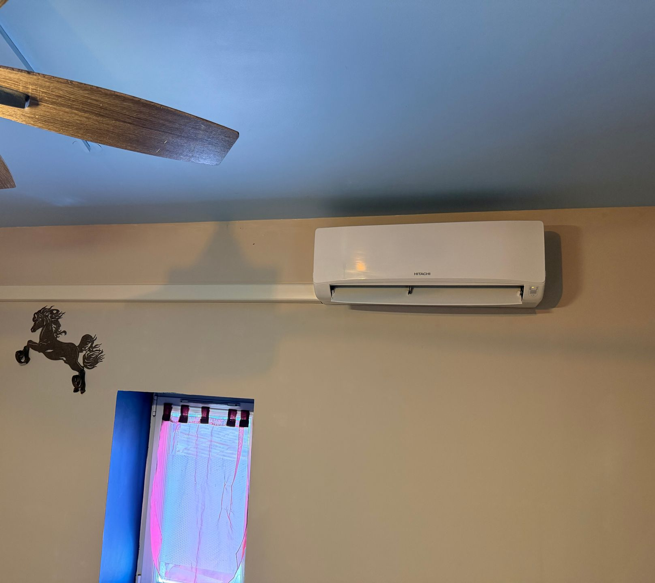 Salon avec climatiseur contre un mur, plafond et petite fenêtre avec rideau.