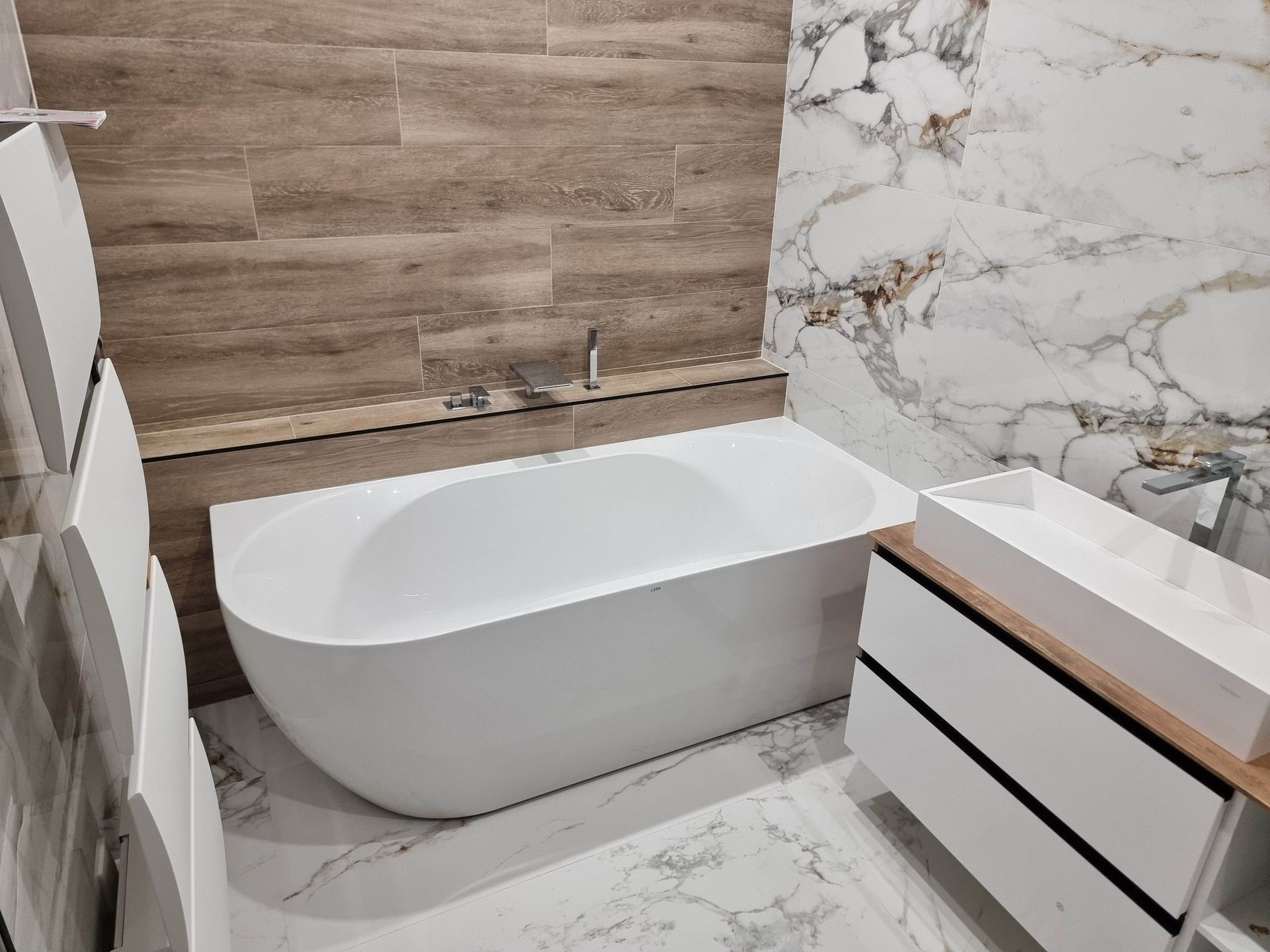 Salle de bains moderne avec baignoire en îlot, mur en marbre, éléments en bois et meuble lavabo suspendu.