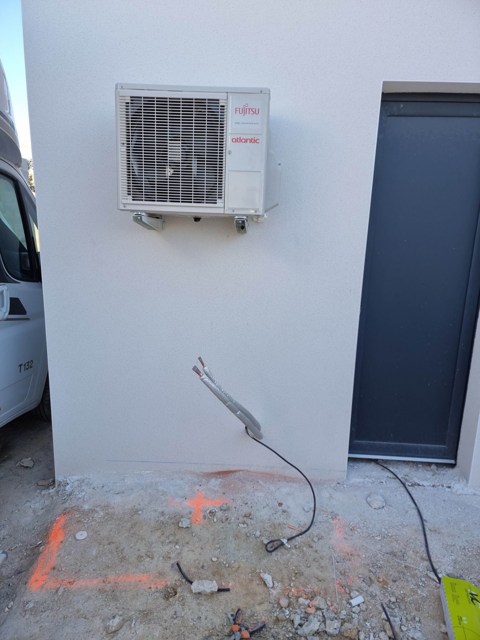 Climatiseur mural à côté d'une porte contre un mur extérieur, avec des gravats au sol.