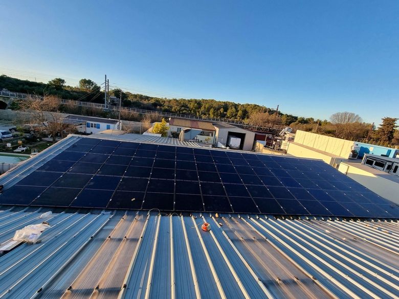 Des panneaux solaires installés sur un toit métallique, avec une colline boisée en arrière-plan.
