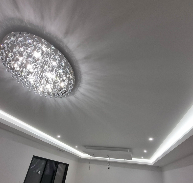 Plafond moderne avec lustre en cristal et spots encastrés dans une pièce.