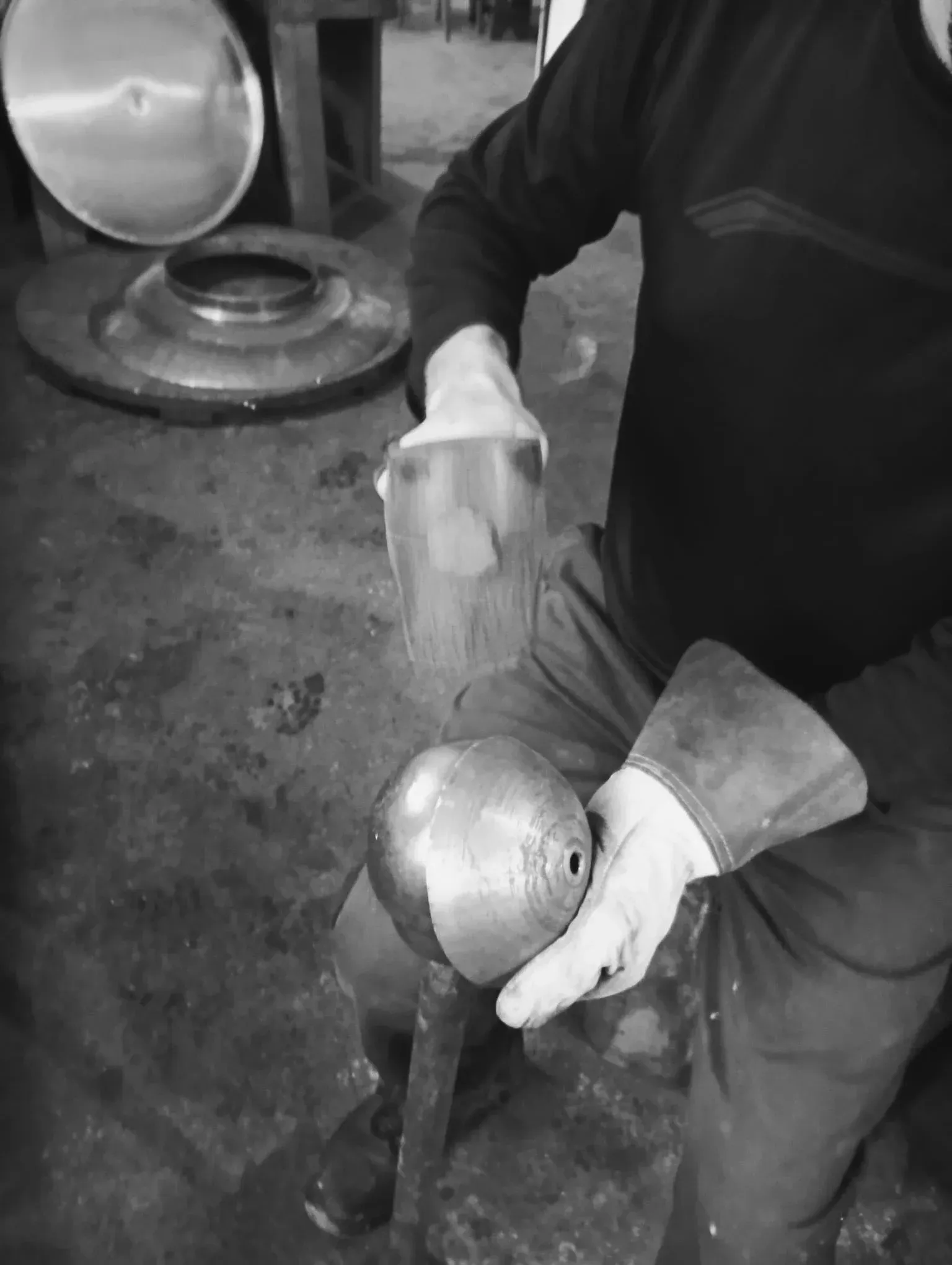 Persona dando forma a una esfera de metal con un martillo en el taller; guantes de protección.