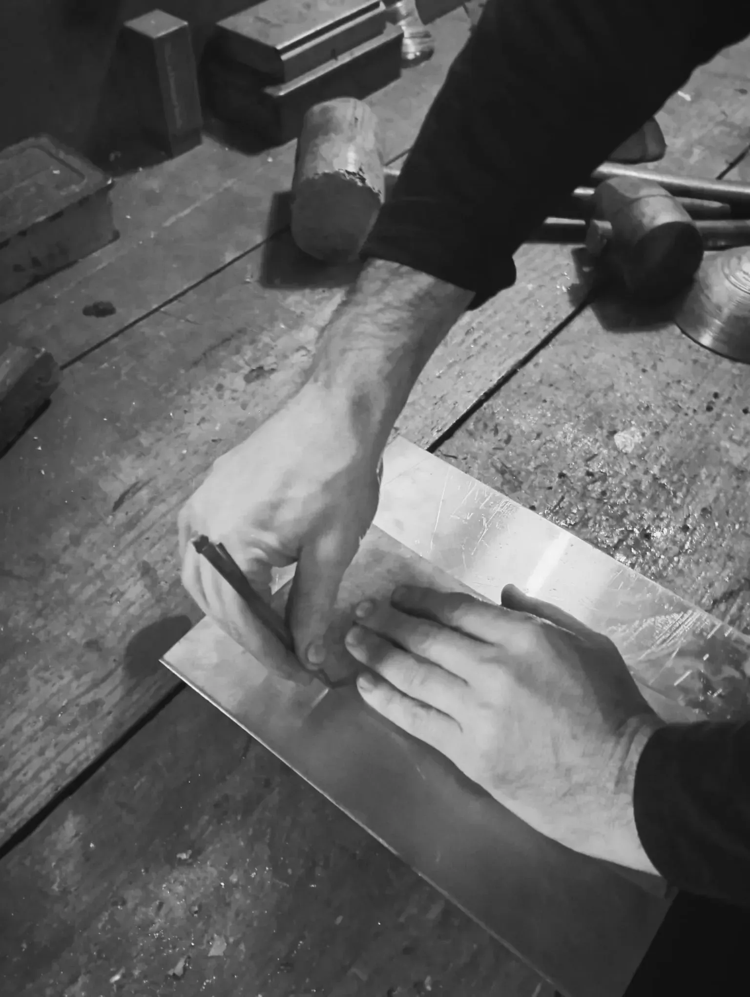 Manos trabajando chapa metálica con una herramienta en un taller.