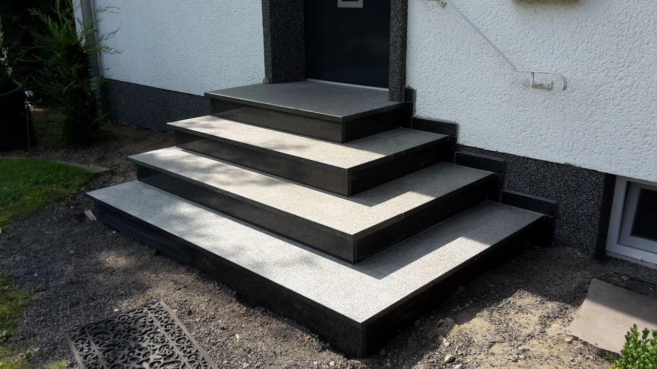 Betontreppe am Hauseingang, dunkle Zierleisten und weiße Wände.