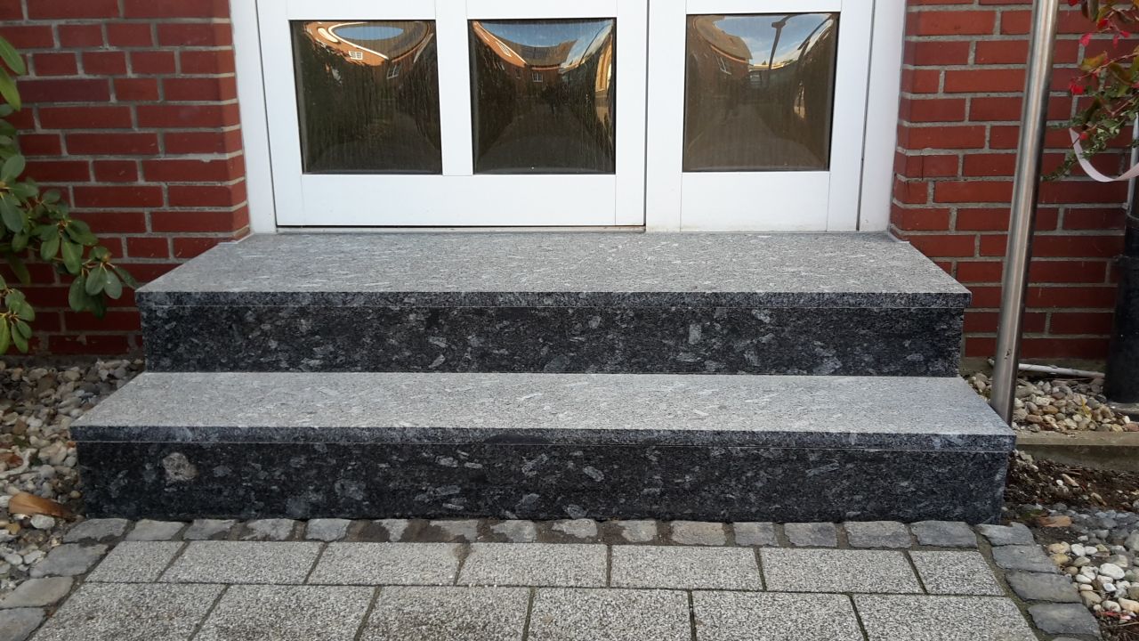 Backsteintür mit schwarzen Steinstufen, die zu weißen Doppeltüren hinaufführen.