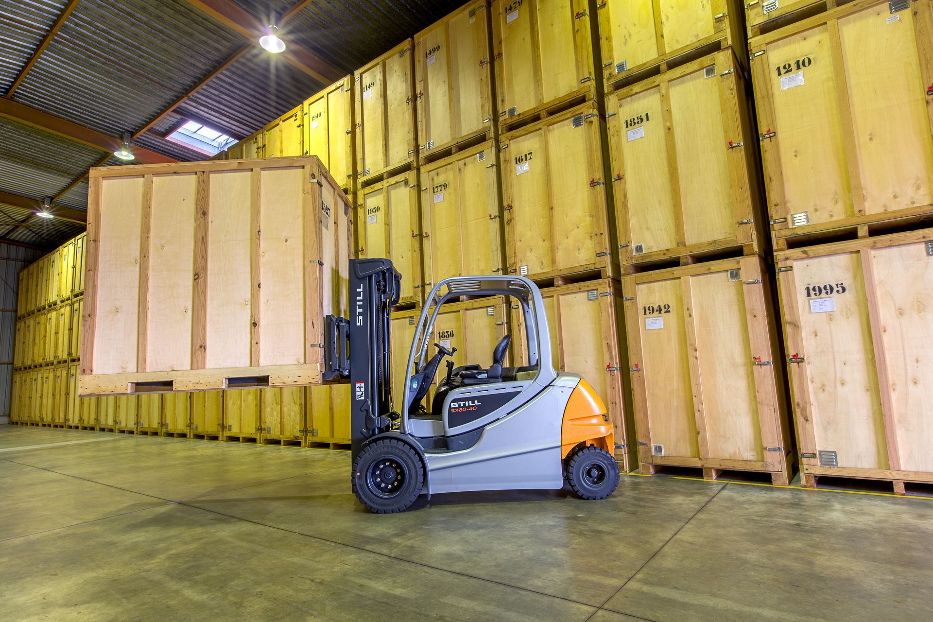 Un box de stockage rempli de meubles emballés dans des cartons, de chaises et de lampes, le long d’une allée étroite.