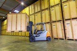 Chariot élévateur jaune dans un entrepôt, à côté de palettes et de cartons empilés