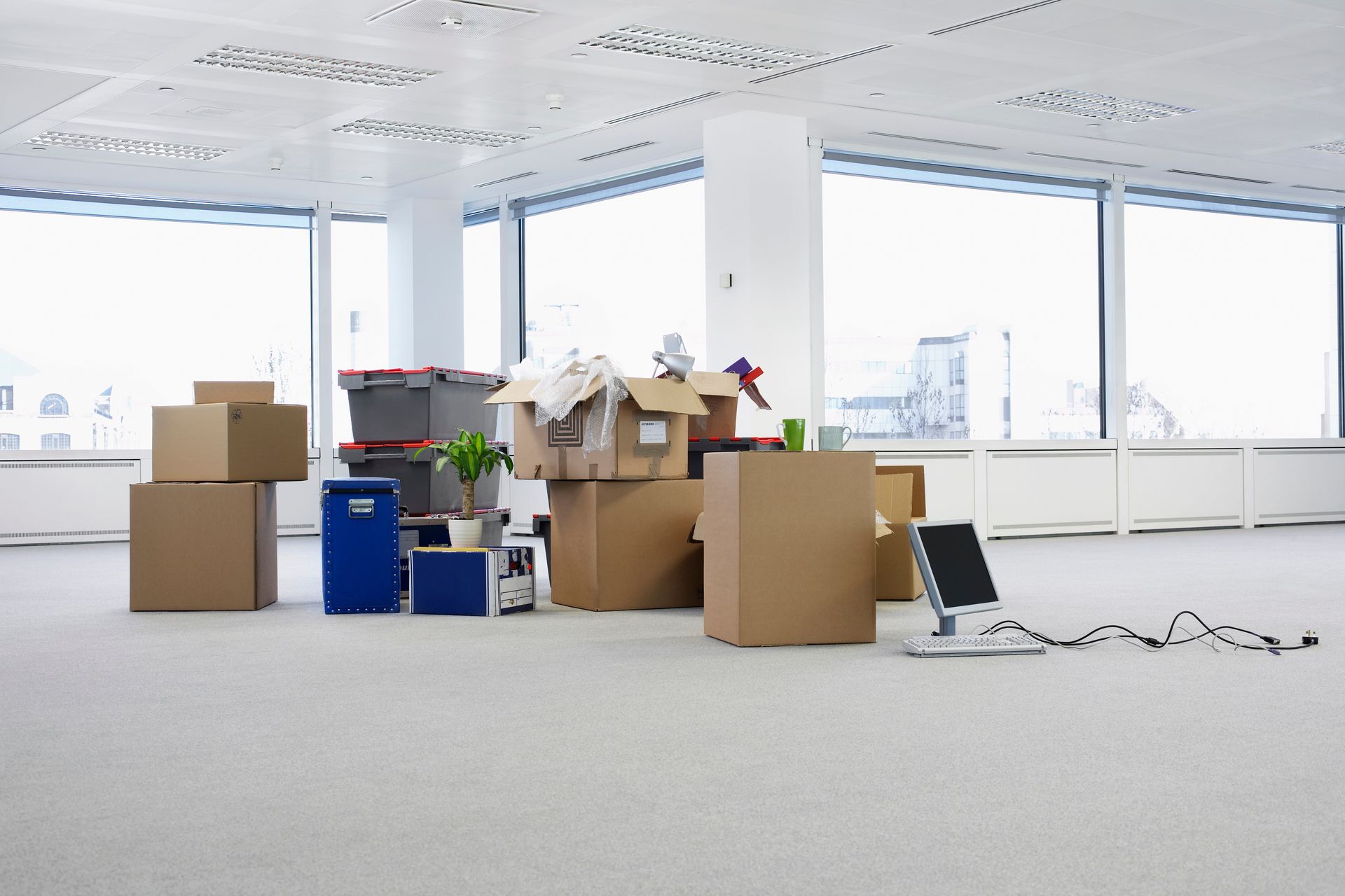 Des cartons de déménagement déballés et un ordinateur portable dans un bureau lumineux et vide aux grandes fenêtres.