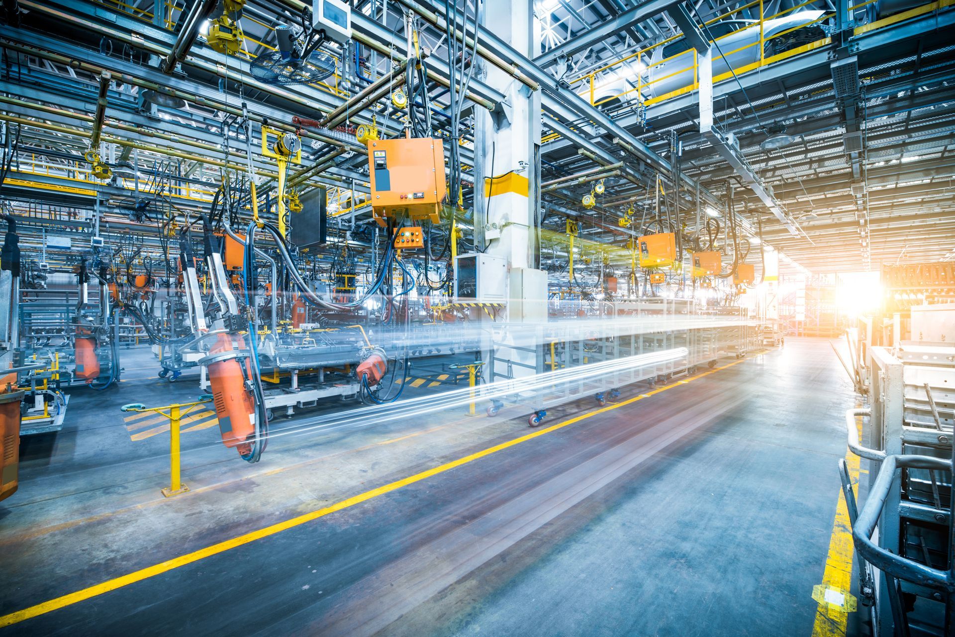 Sol lumineux d’une usine industrielle, avec des ouvriers, des machines et des rayons de soleil venant de la droite.