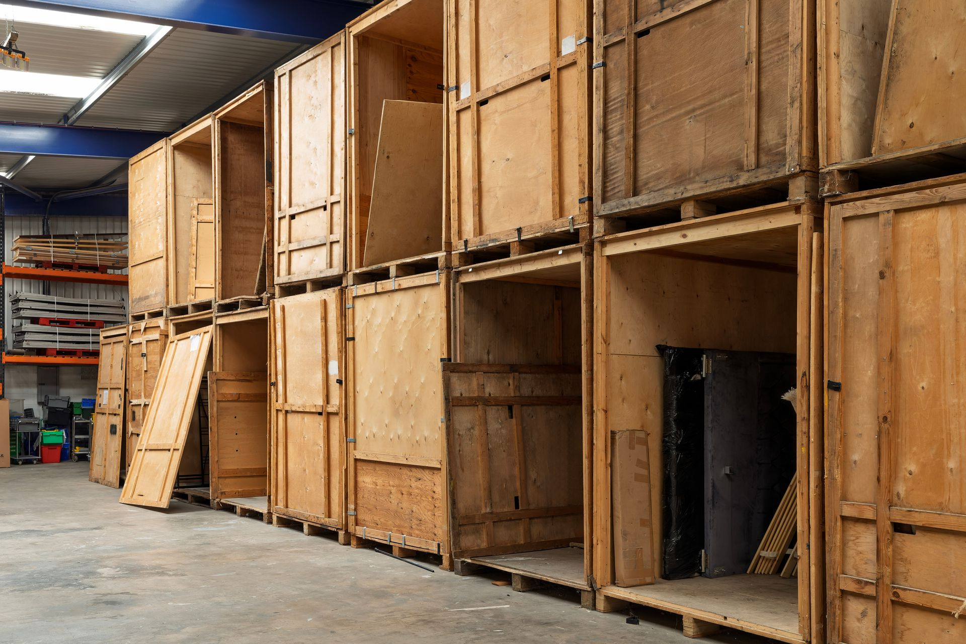Allée d’entrepôt avec des caisses et des palettes en bois empilées le long du mur.