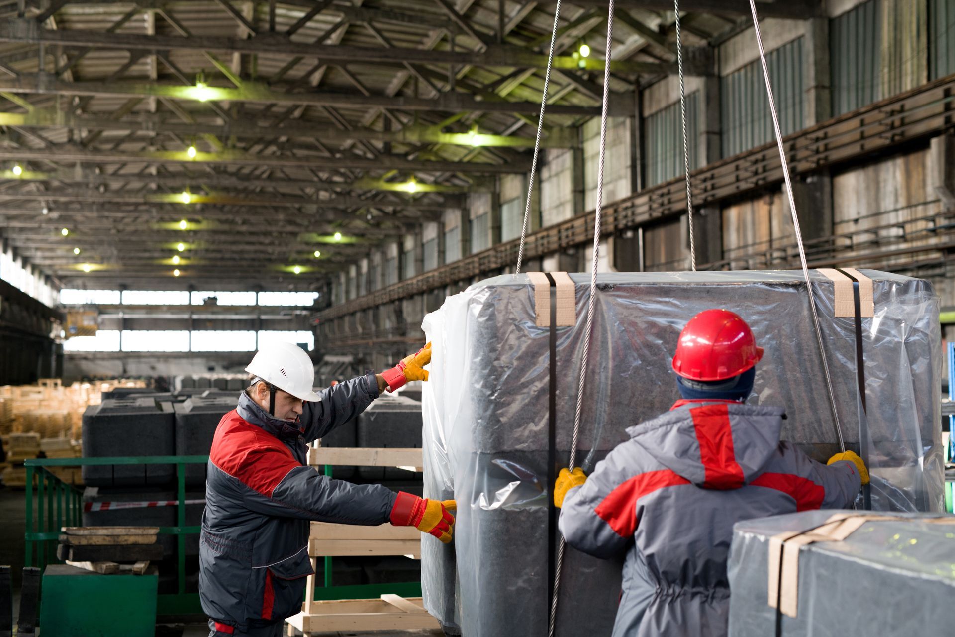 Des ouvriers portant des casques de chantier déplacent du matériel industriel emballé dans un entrepôt.