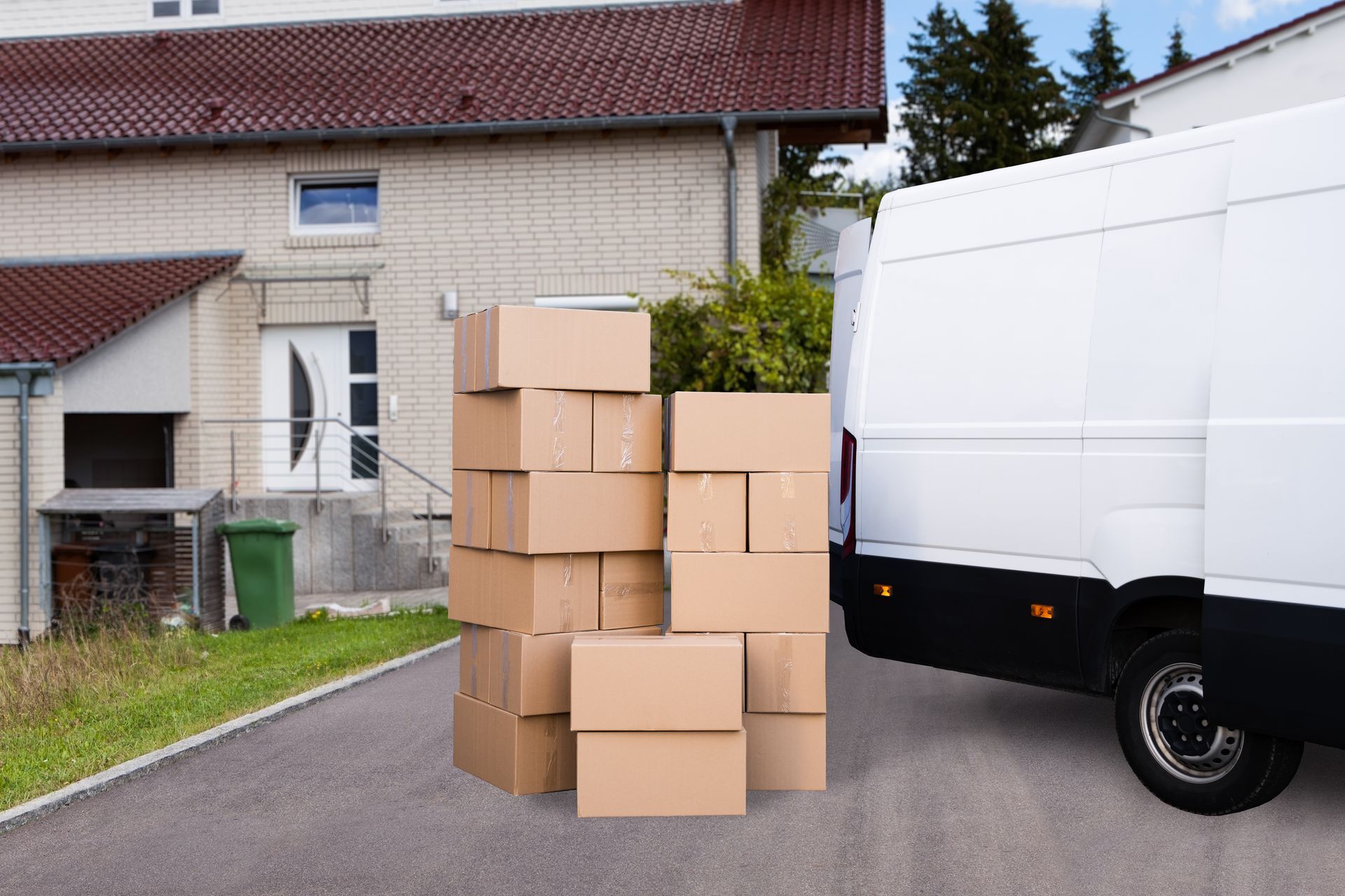 Des piles de cartons à côté d’une camionnette de livraison blanche, dans une allée près d’une maison.