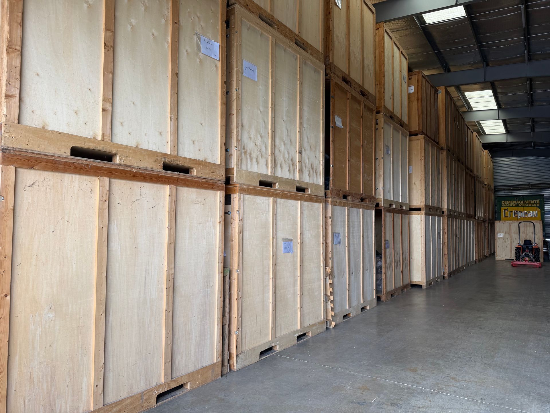 Un box de stockage rempli de cartons, de pneus, d’étagères, d’une chaise recouverte d’une housse et de vélos suspendus.