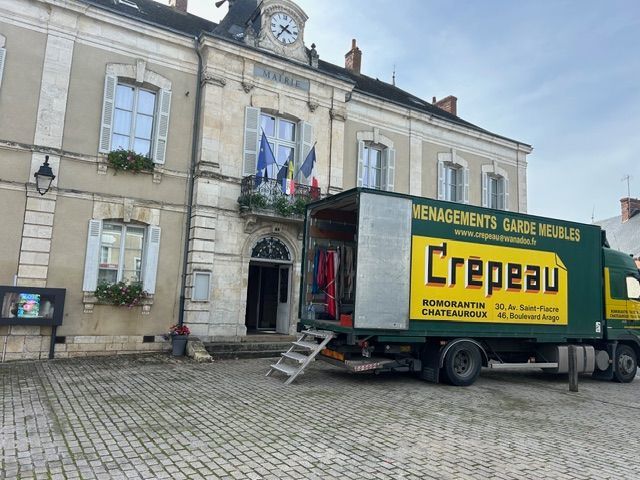 Une personne charge un camion à l’aide d’une rampe, en portant un matelas plié dans l’espace de chargement ouvert.