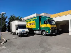 Deux semi-remorques, l’un vert et jaune, l’autre blanc, stationnés devant un bâtiment ensoleillé.