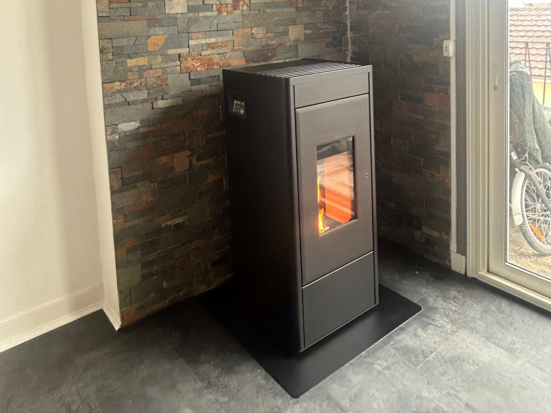 Poêle à granulés noir devant un mur en pierre, avec des flammes brûlantes visibles